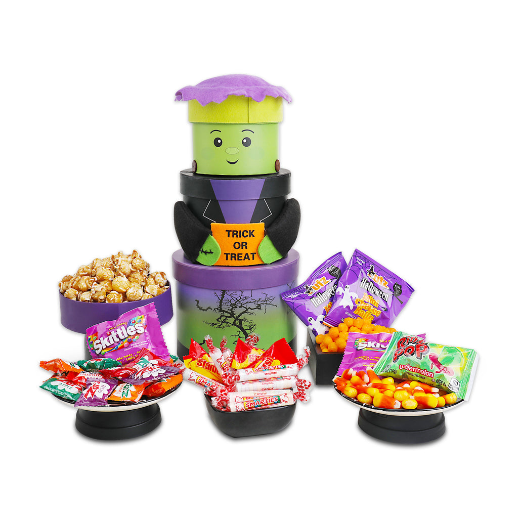 A Halloween-themed candy and snack display set on a white background, featuring a purple and green Frankenstein-themed candy dispenser with a 'TRICK OR TREAT' sign, surrounded by bowls and plates of assorted candy.