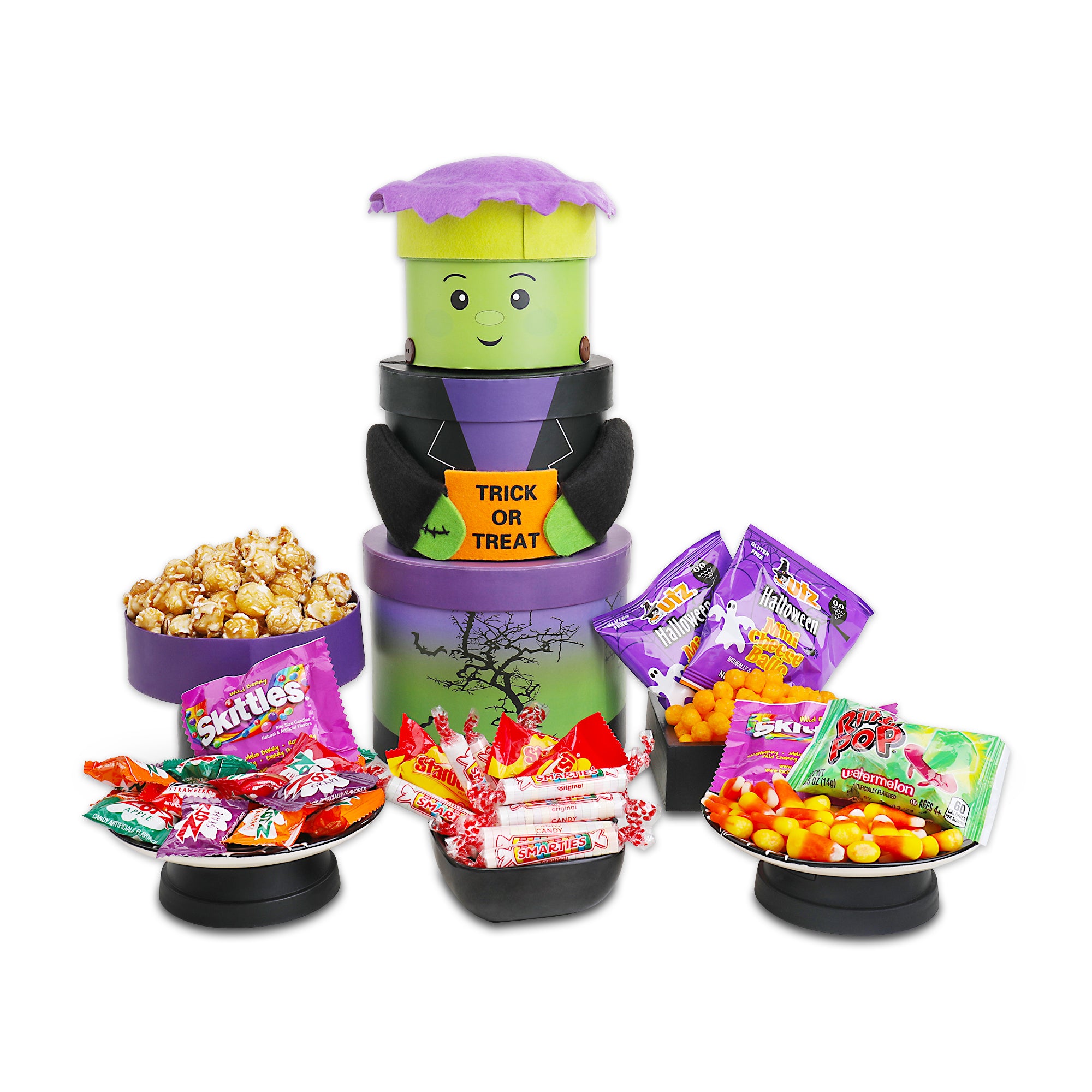 A Halloween-themed candy and snack display set on a white background, featuring a purple and green Frankenstein-themed candy dispenser with a 'TRICK OR TREAT' sign, surrounded by bowls and plates of assorted candy.