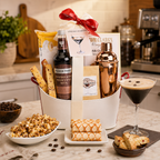 Gift basket with coffee-themed items including a bottle of Fever-Tree mix, a cocktail shaker, and a glass of espresso martini on a kitchen counter.