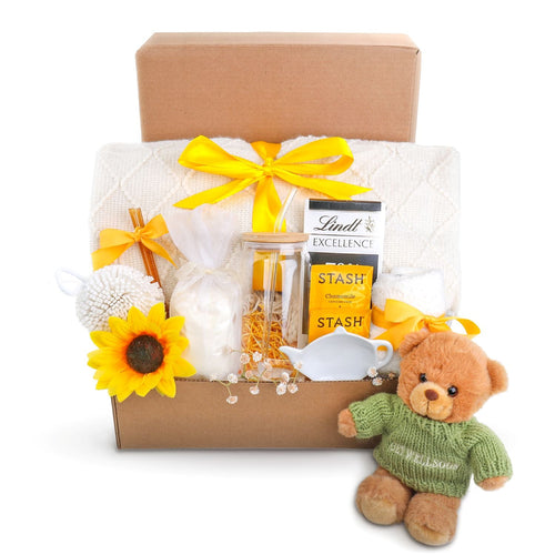 Gift basket with teddy bear, tea set, and snacks on a white background